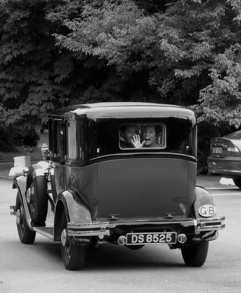 happy couple waves goodbye out the back window of an old car