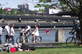 A couple riding a tandem bike in the waterfront park with balloons trailing out behind them